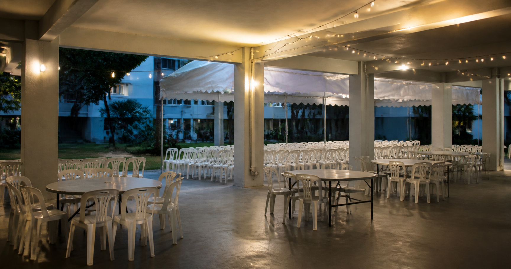 An HDB void deck in Singapore set up with white chairs and a canopy for a funeral wake