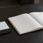 A plain white envelope and a pen on a dark table beside an open condolence book